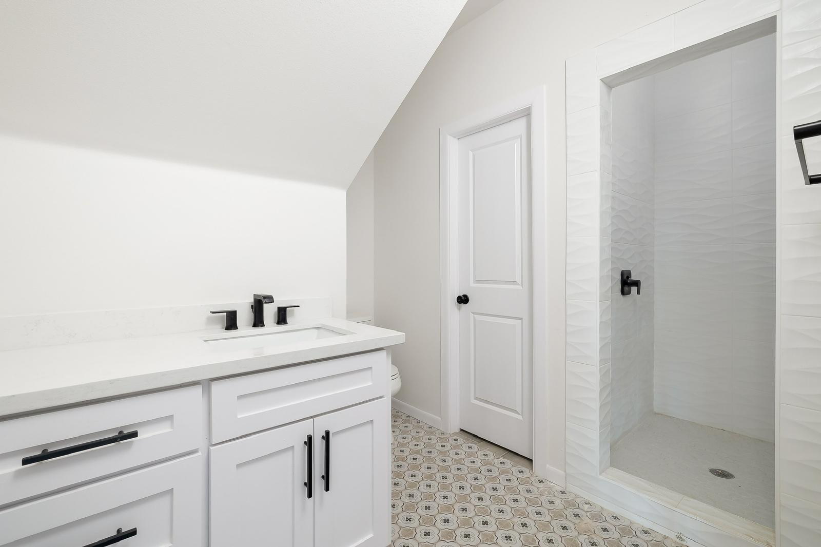 Cassandra Row · bath with sloped ceiling, walk in shower and patterned tile floor